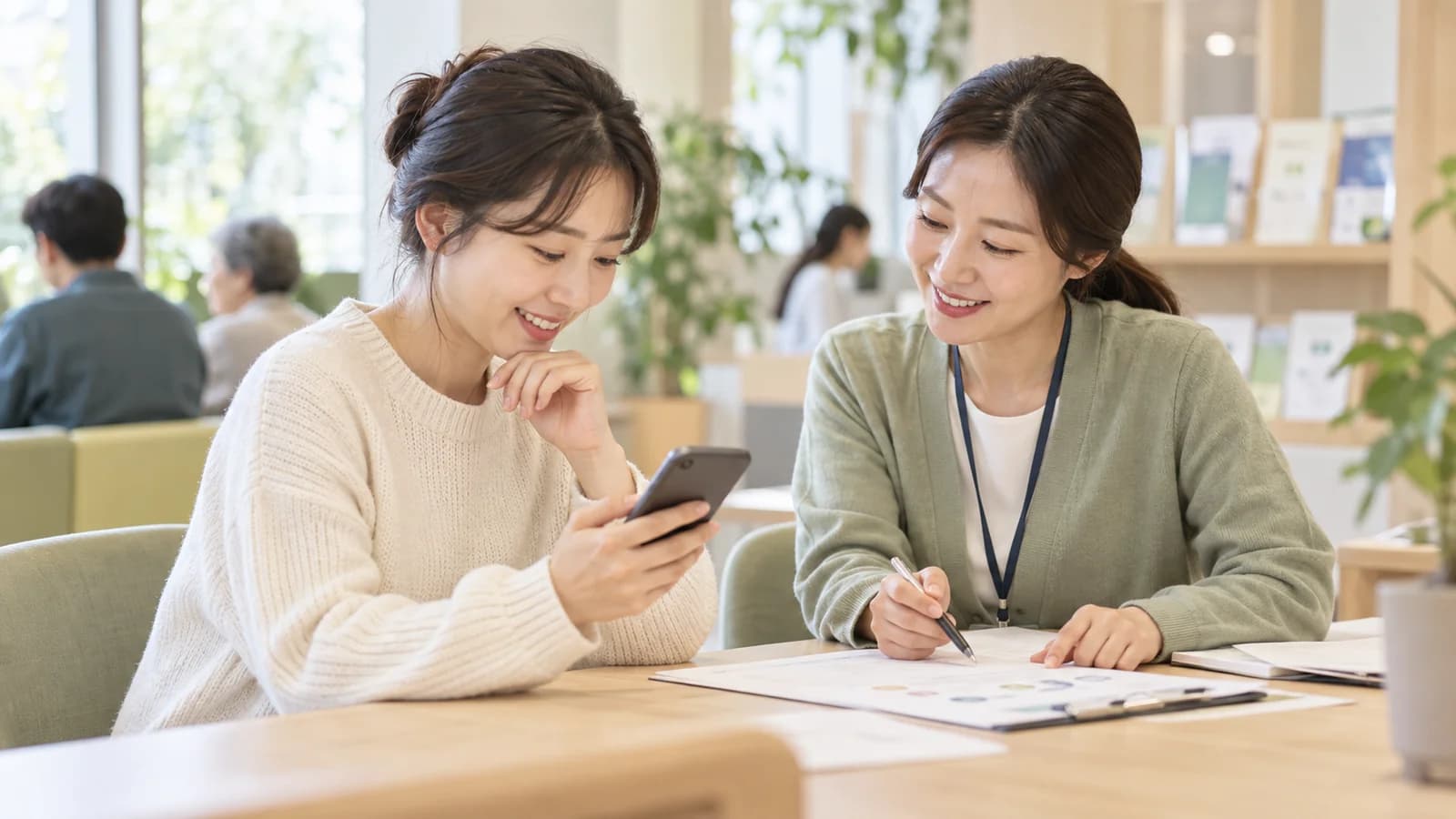 공공서비스 상담 공간에서 안내 직원과 함께 스마트폰으로 맞춤 지원 정보를 확인하는 이용자